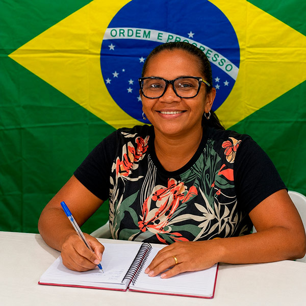 Aluna EJA sorrindo enquanto escreve